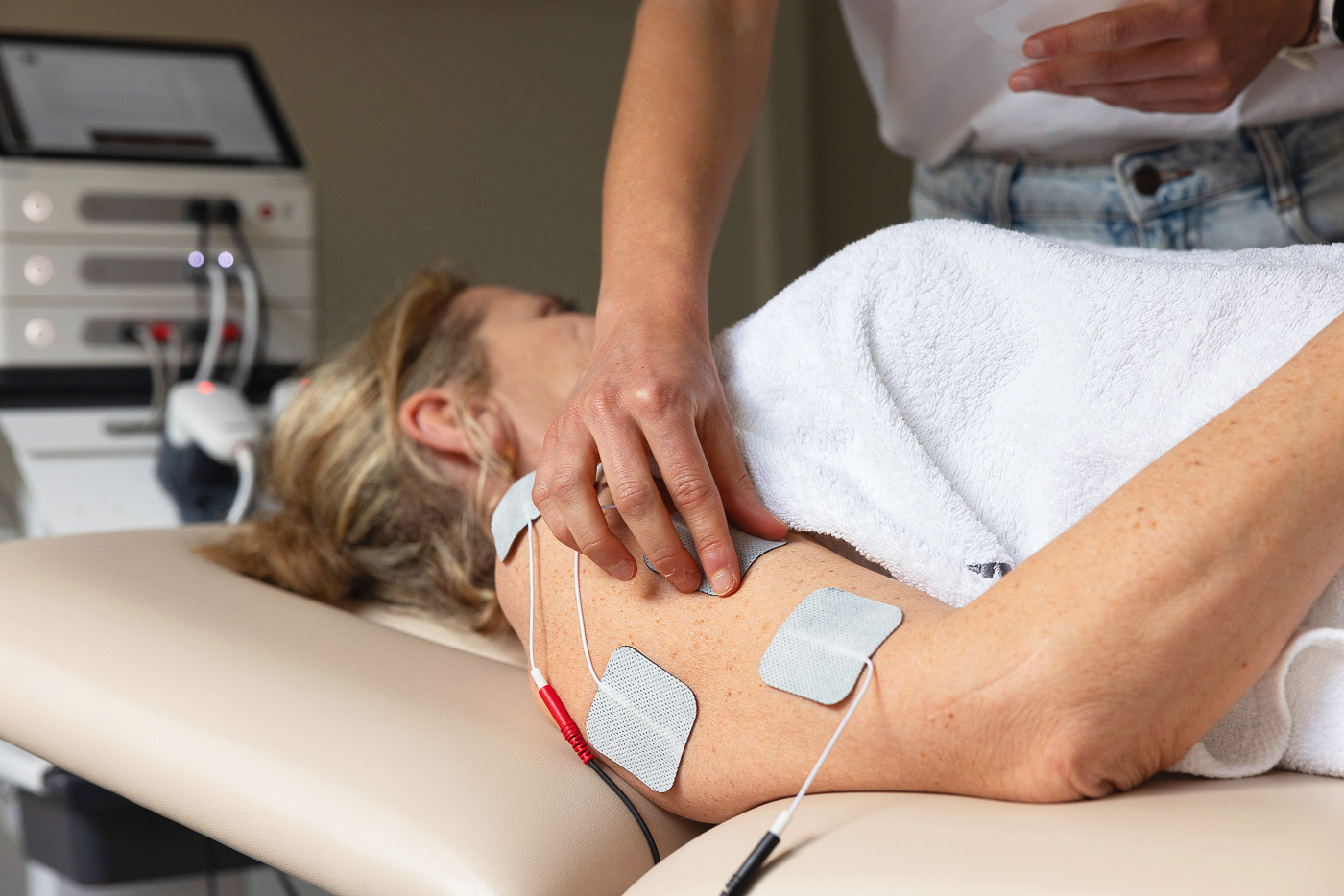 A patient is lying on the treatment table, electrodes are attached to their arm.